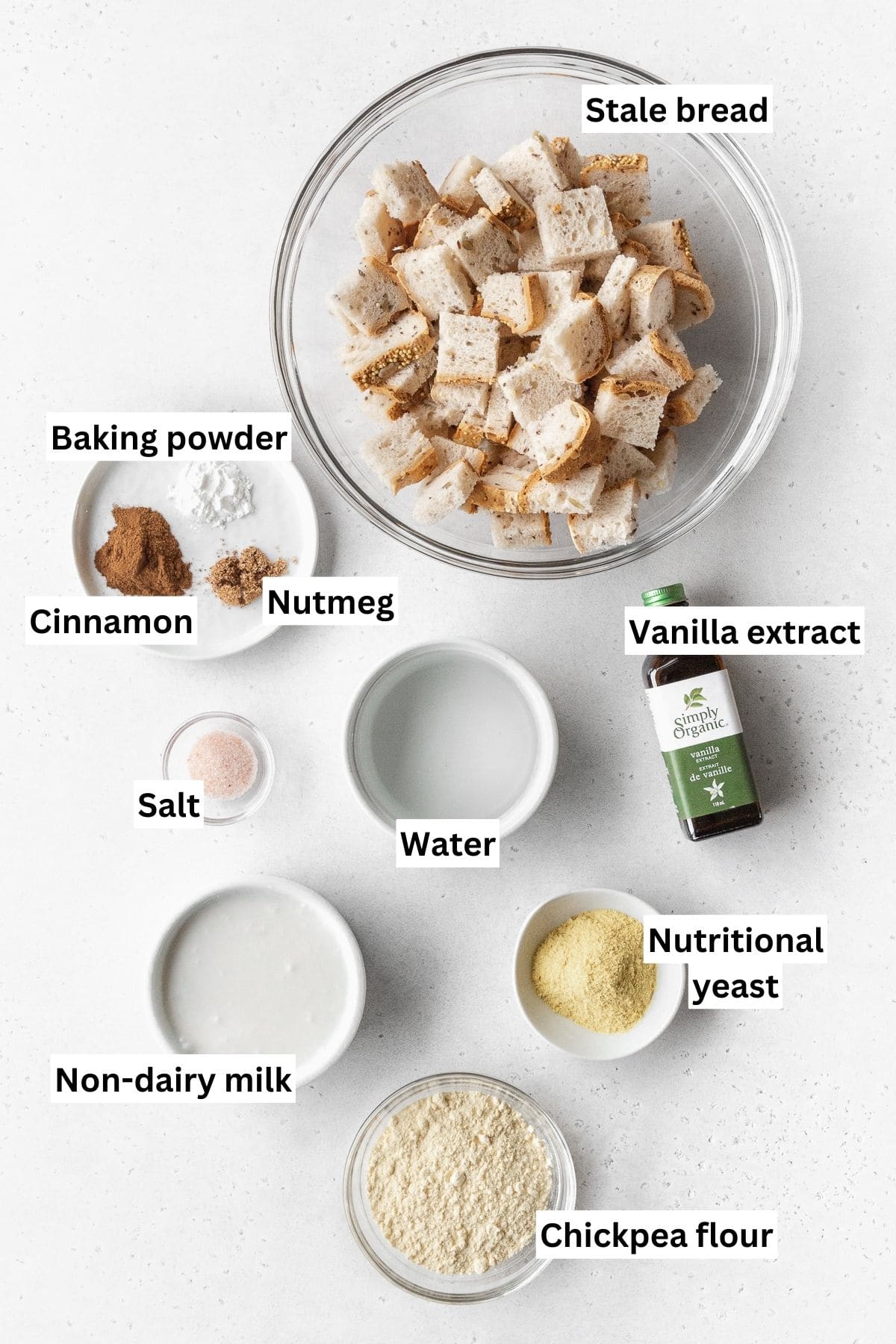 Overhead shot of vegan bread pudding ingredients measured out into small bowls on a white surface.