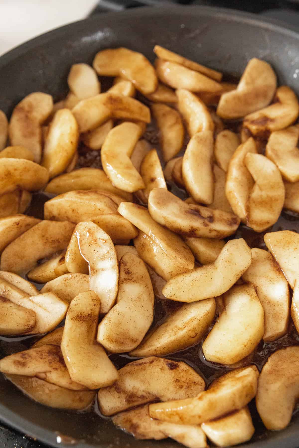 Sliced apples coated in apple pie spice cooking in a black pan.