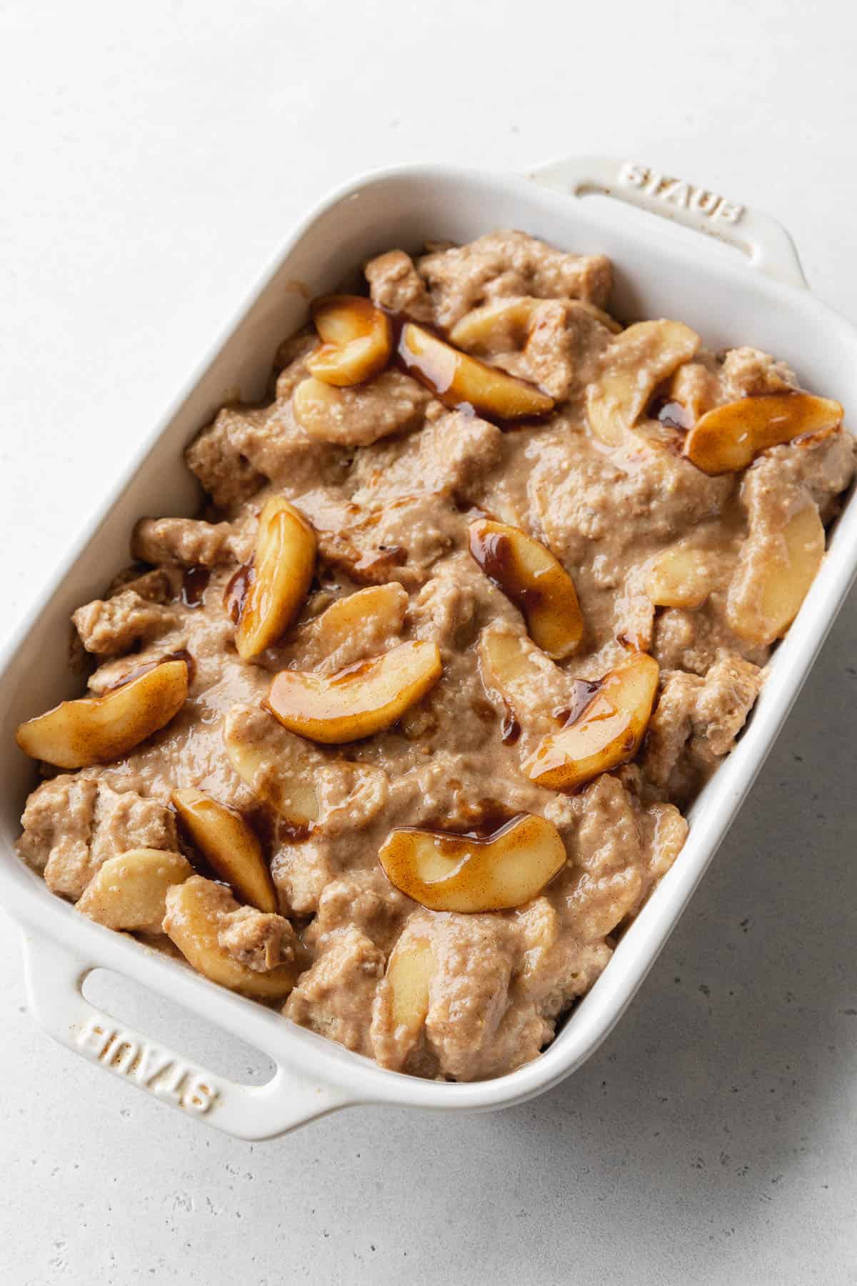 Vegan apple pie bread pudding in a white casserole dish ready to be baked.