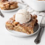 Slice of apple pie vegan bread pudding on a white dessert plate, topped with a scoop of vegan ice cream.