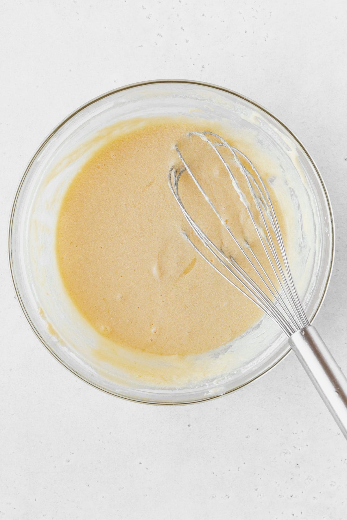 Lemon curd ingredients mixed together in a glass bowl with a whisk.