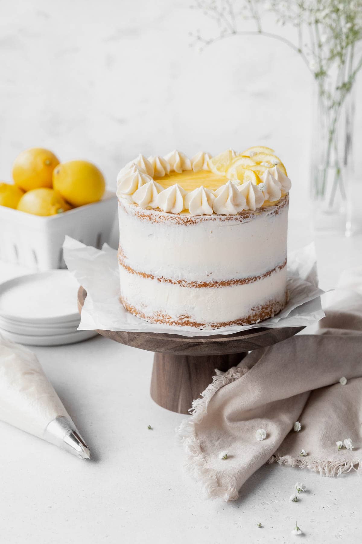 Final flourishes added to the dairy-free lemon curd cake including rosettes of lemon buttercream, a center topping of lemon curd, and candied lemons as decoration.