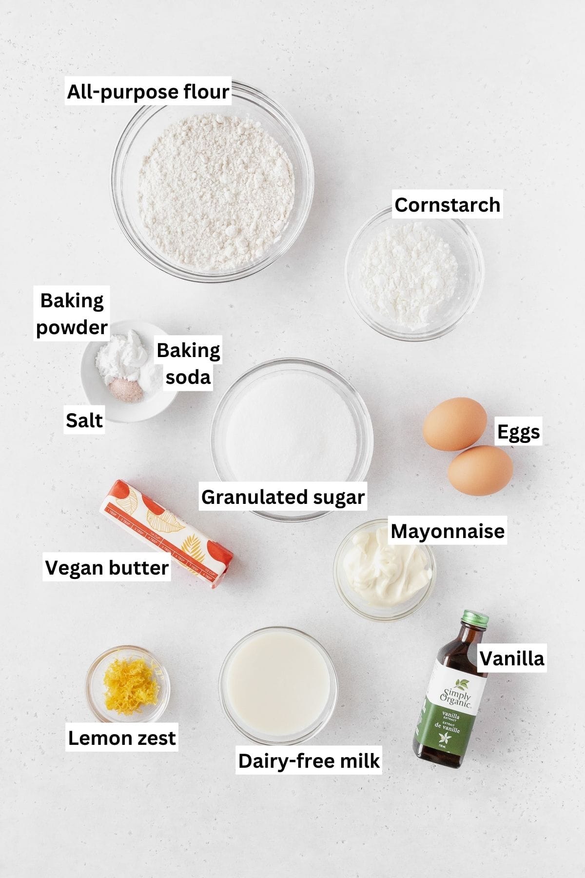 Ingredients needed for making dairy-free lemon layer cakes on a white table with text overlay.