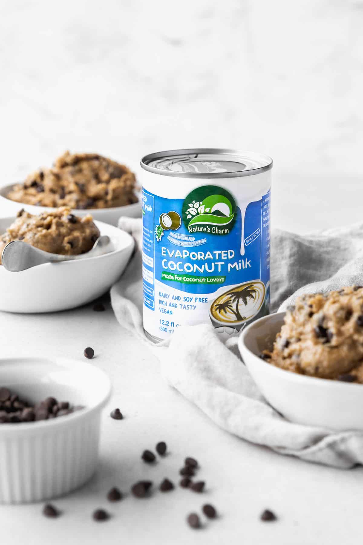 Can of Nature's Charm evaporated coconut milk in the center of an array of bowls filled with vegan edible cookie dough.