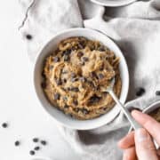 Square hero of vegan dairy-free edible cookie dough in a bowl with a hand taking a spoonful.