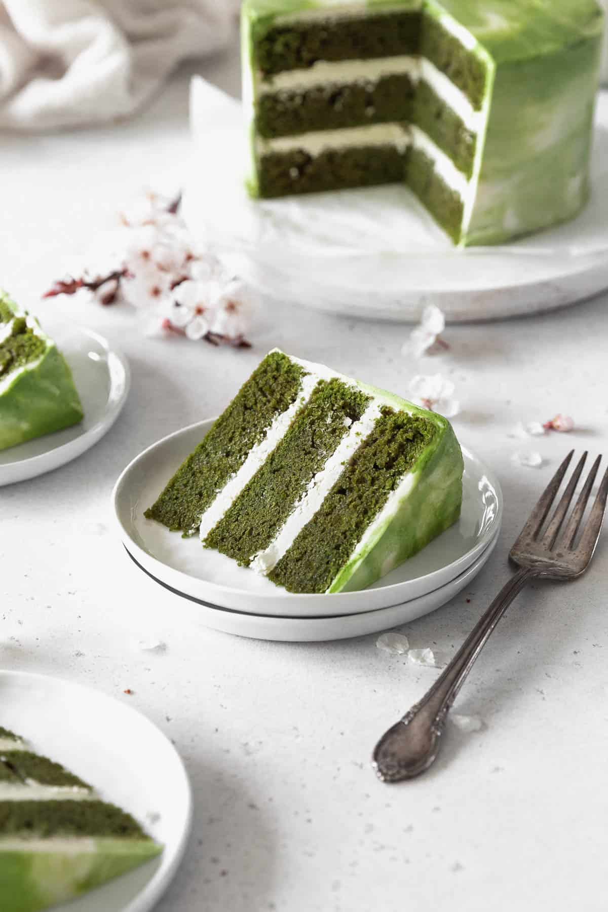 A piece of matcha cake on a white dessert plate next to a fork.