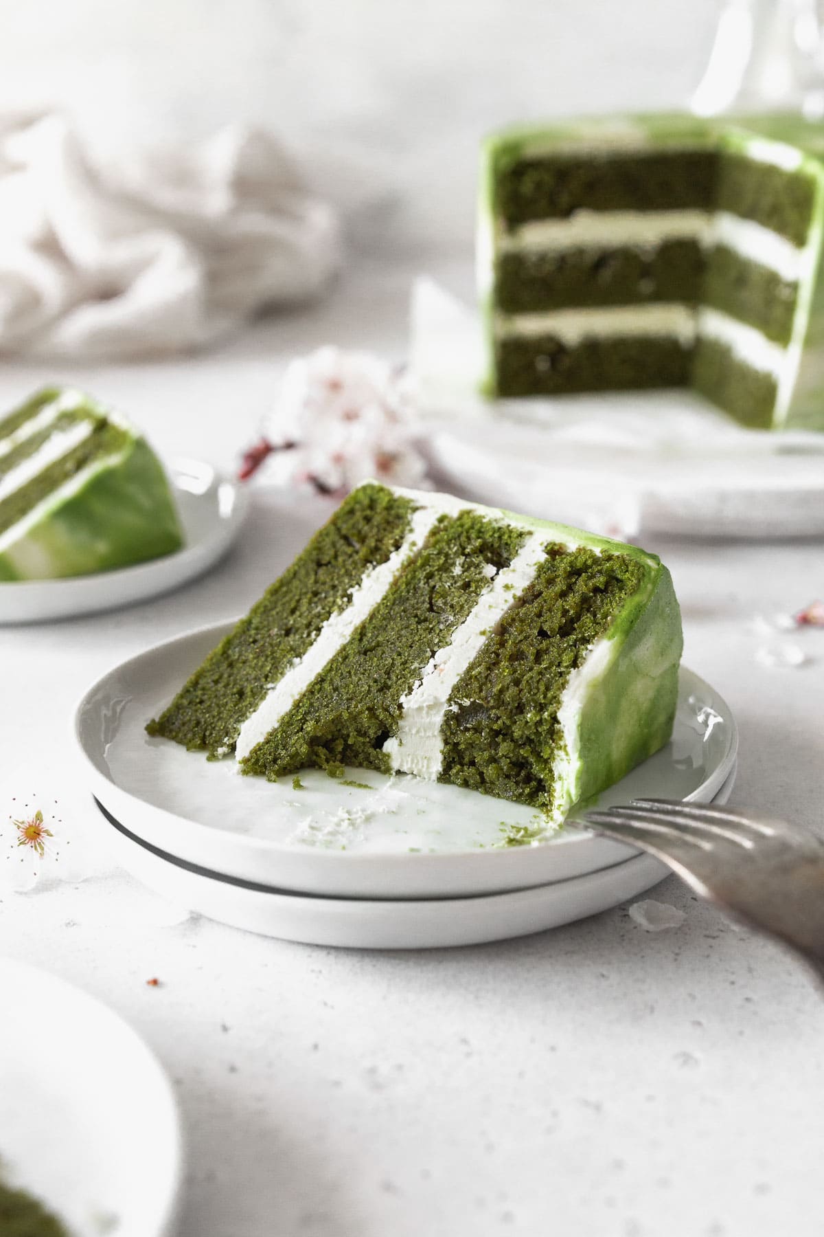 An up-close shot of a piece of matcha cake on a dessert plate with a bite taken out of it. 