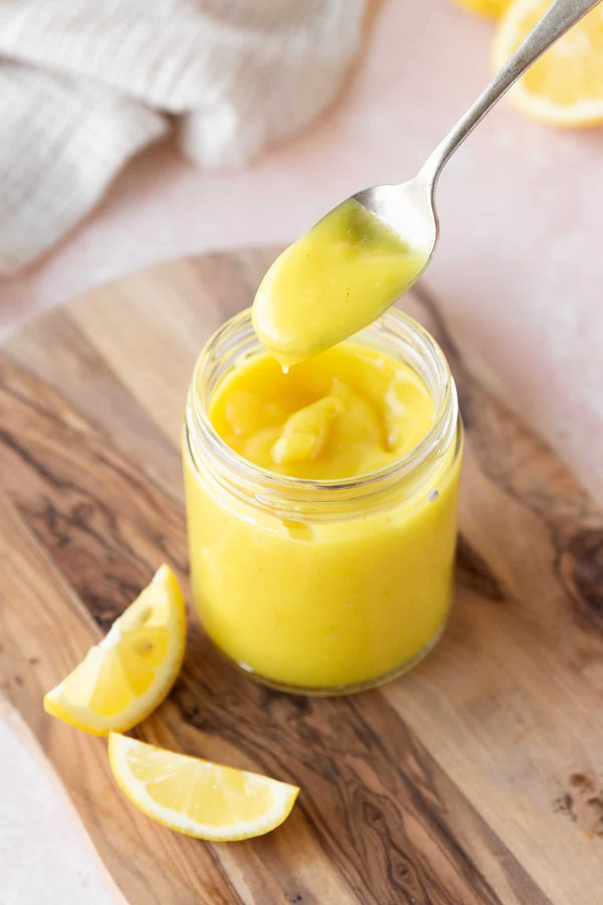 45 degree angle shot of a spoonful of vegan lemon curd above the mason jar to show the thick consistency.