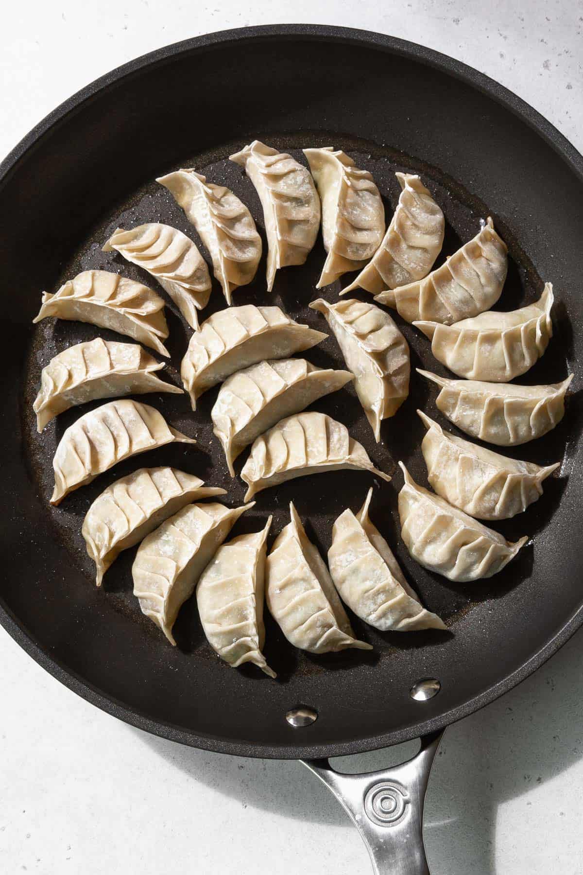 Uncooked gyoza lined on a greased nonstick frying pan.