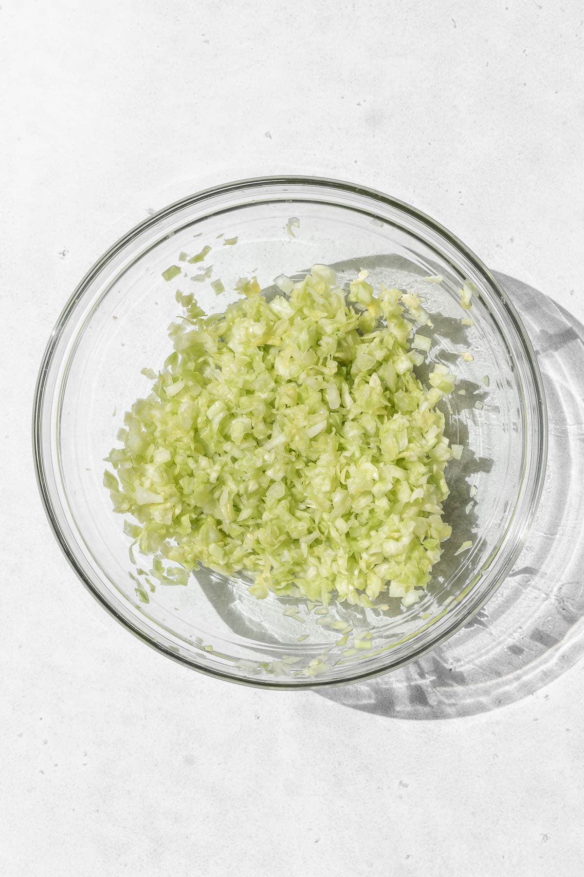 Minced cabbage in a glass bowl on a white surface.