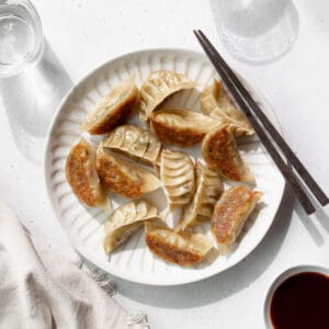 Square hero shot of vegetable gyoza on a white plate with wooden chopsticks.