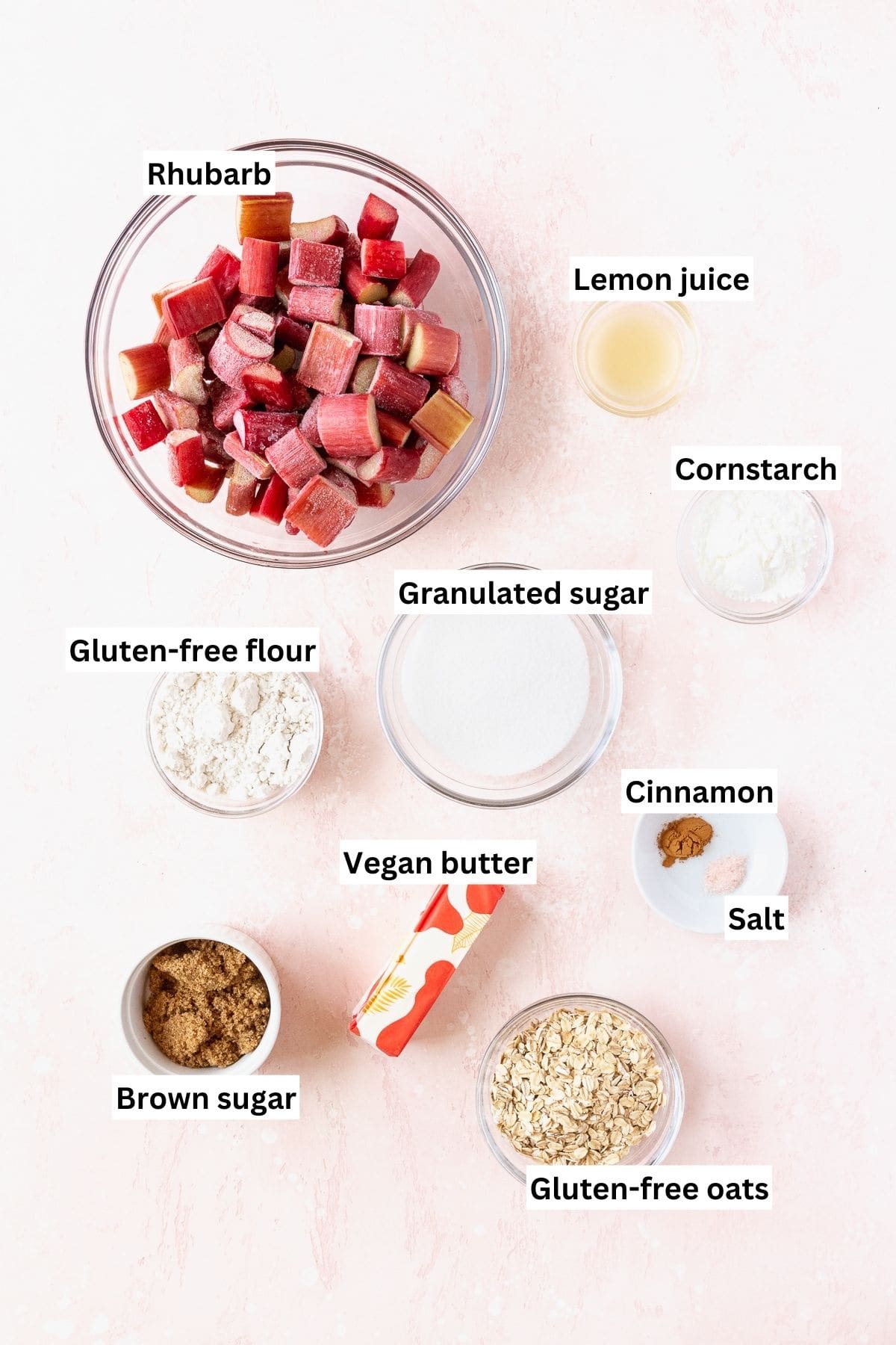 Ingredients needed to make gluten-free rhubarb crisp measured out into bowls on a pink table with text overlay.