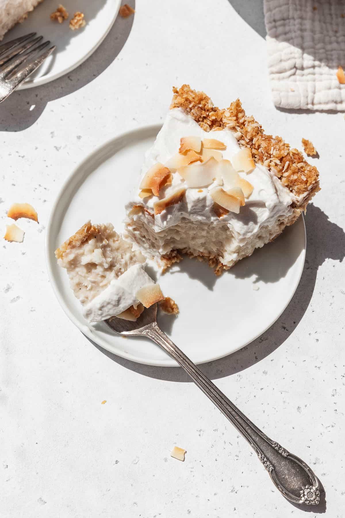 Small white dessert plate with a slice of GF no-bake plant-based coconut cream pie with a silver fork taking a bite out of it.
