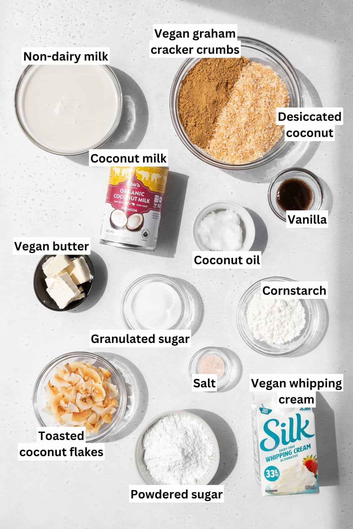 Overhead shot of ingredients needed to make vegan, gluten-free no-bake coconut cream pie measured out into bowls on a white table with text overlay.