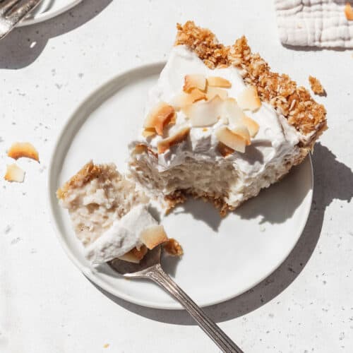 Square hero image of vegan no bake coconut cream pie on a white plate with a fork taking a bite out.