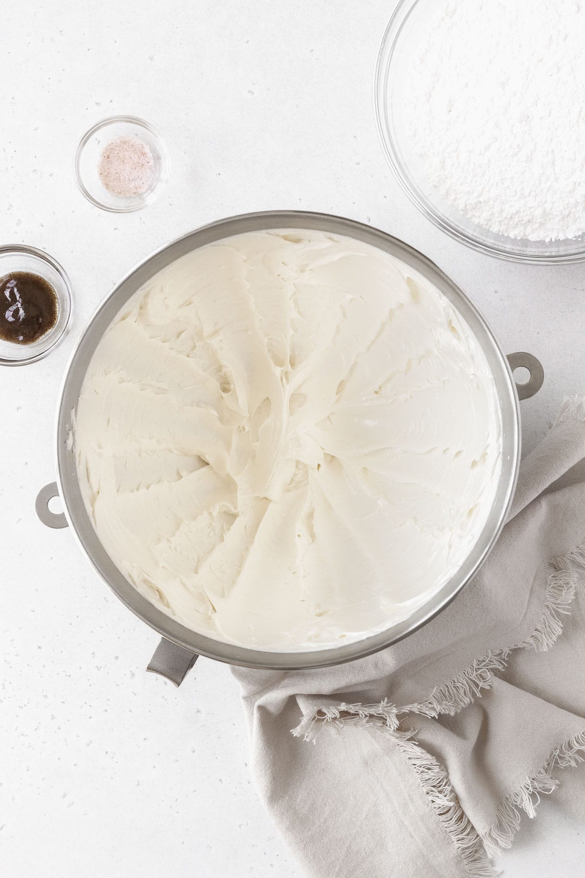 A large mixing bowl of whipped butter next to a bowl of confectioner's sugar and vanilla.