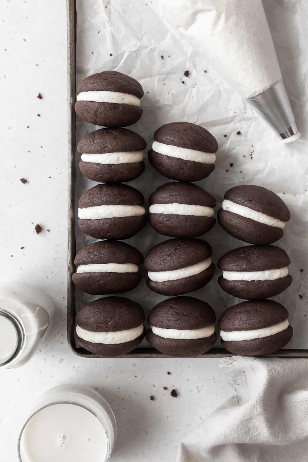 A parchment paper lined baking tray with gluten-free whoopie pies and a piping bag.