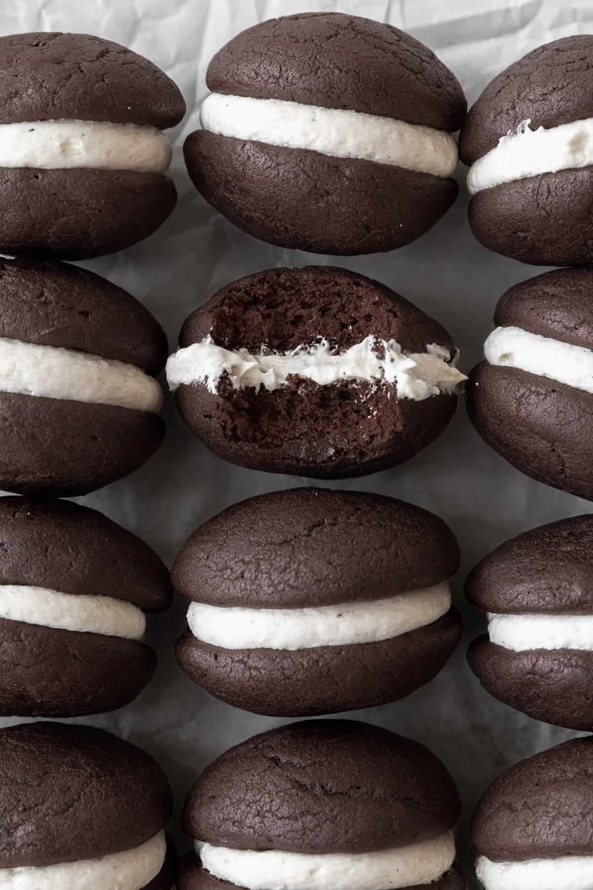Gluten-free whoopie pies on a white sheet of parchment paper. One of the cookies has a bite taken out of it.