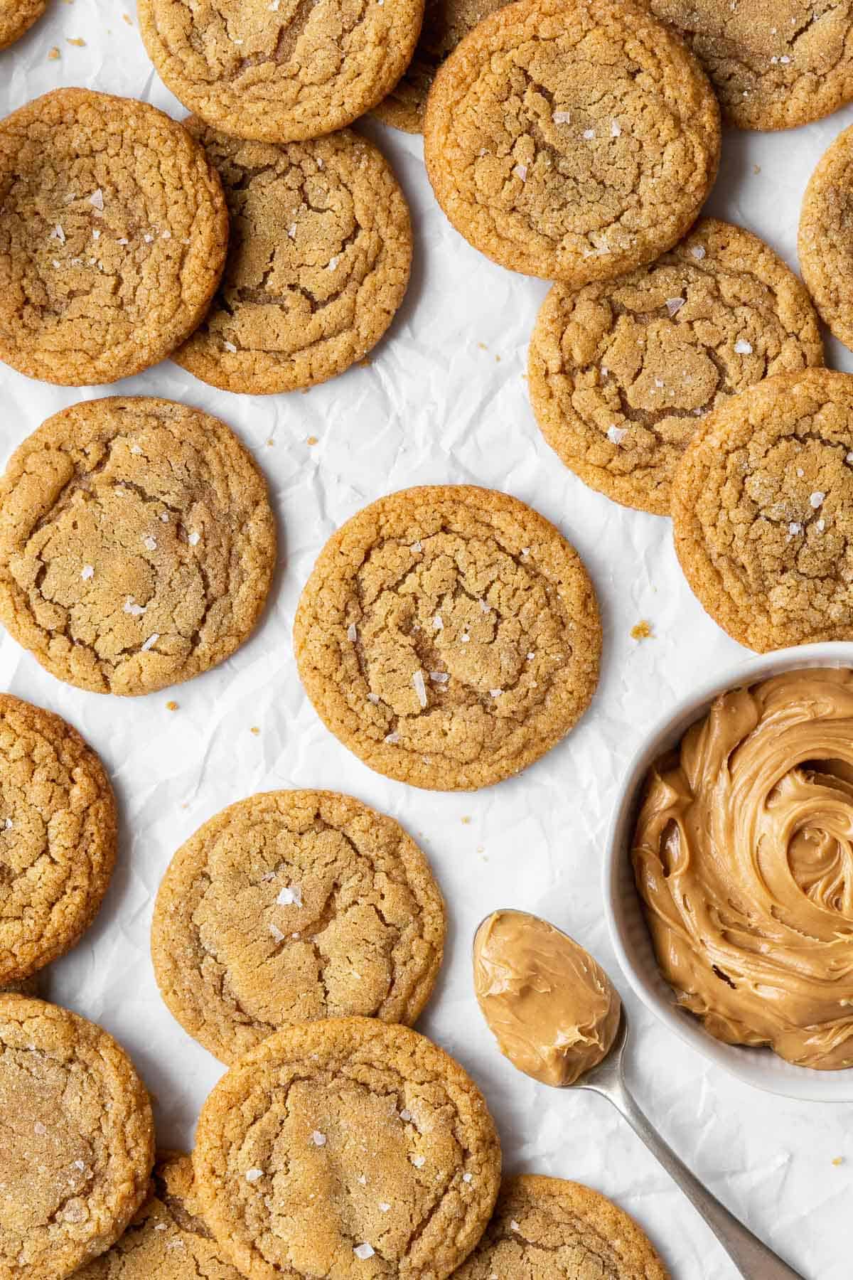 Dairy-free peanut butter cookies on parchment paper with a spoonful and bowl of peanut butter.