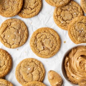 A square shot of dairy-free peanut butter cookies on parchment paper with a bowl of peanut butter on the side.
