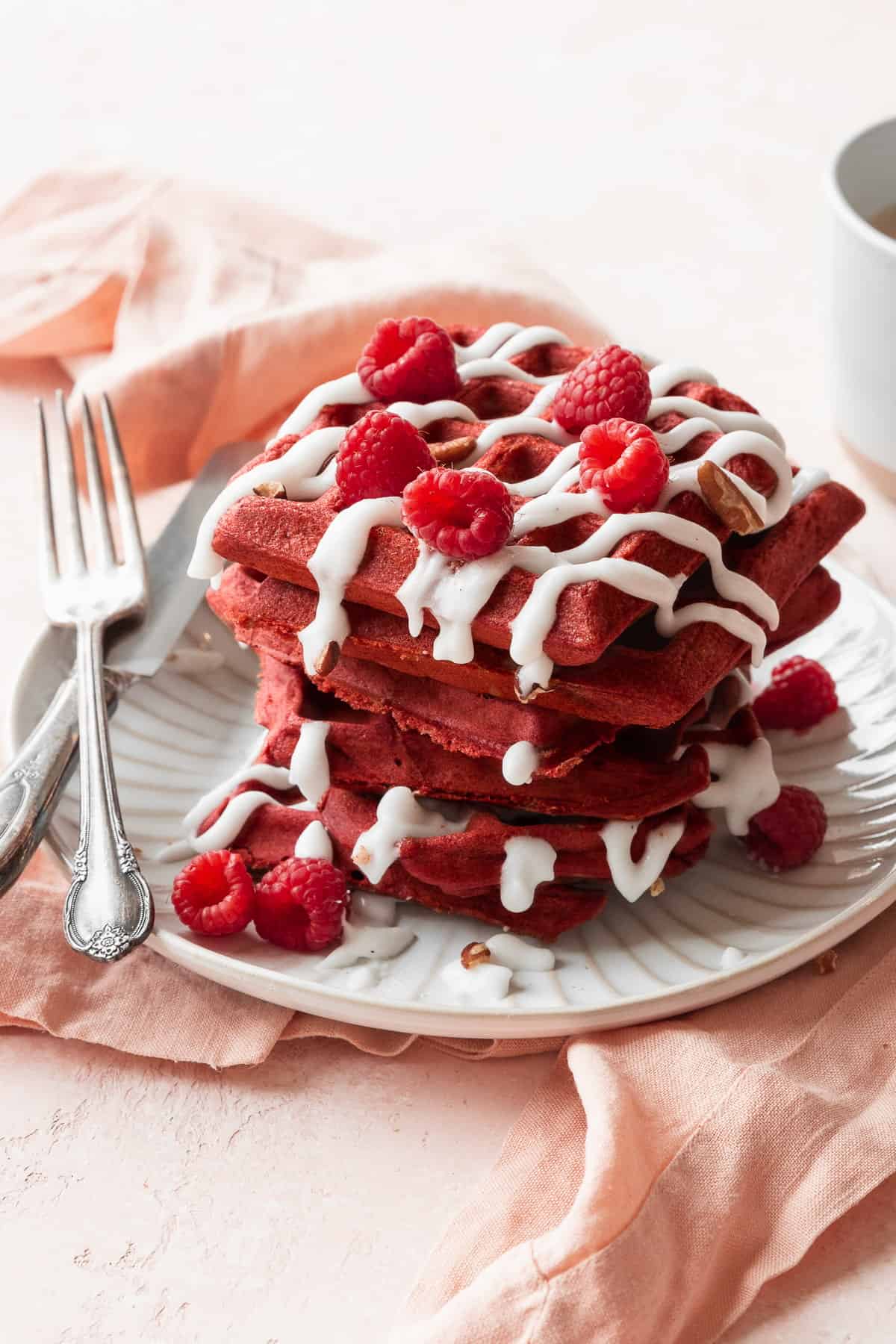 A side shot of a stack of red velvet waffles with cream cheese glaze and raspberries.