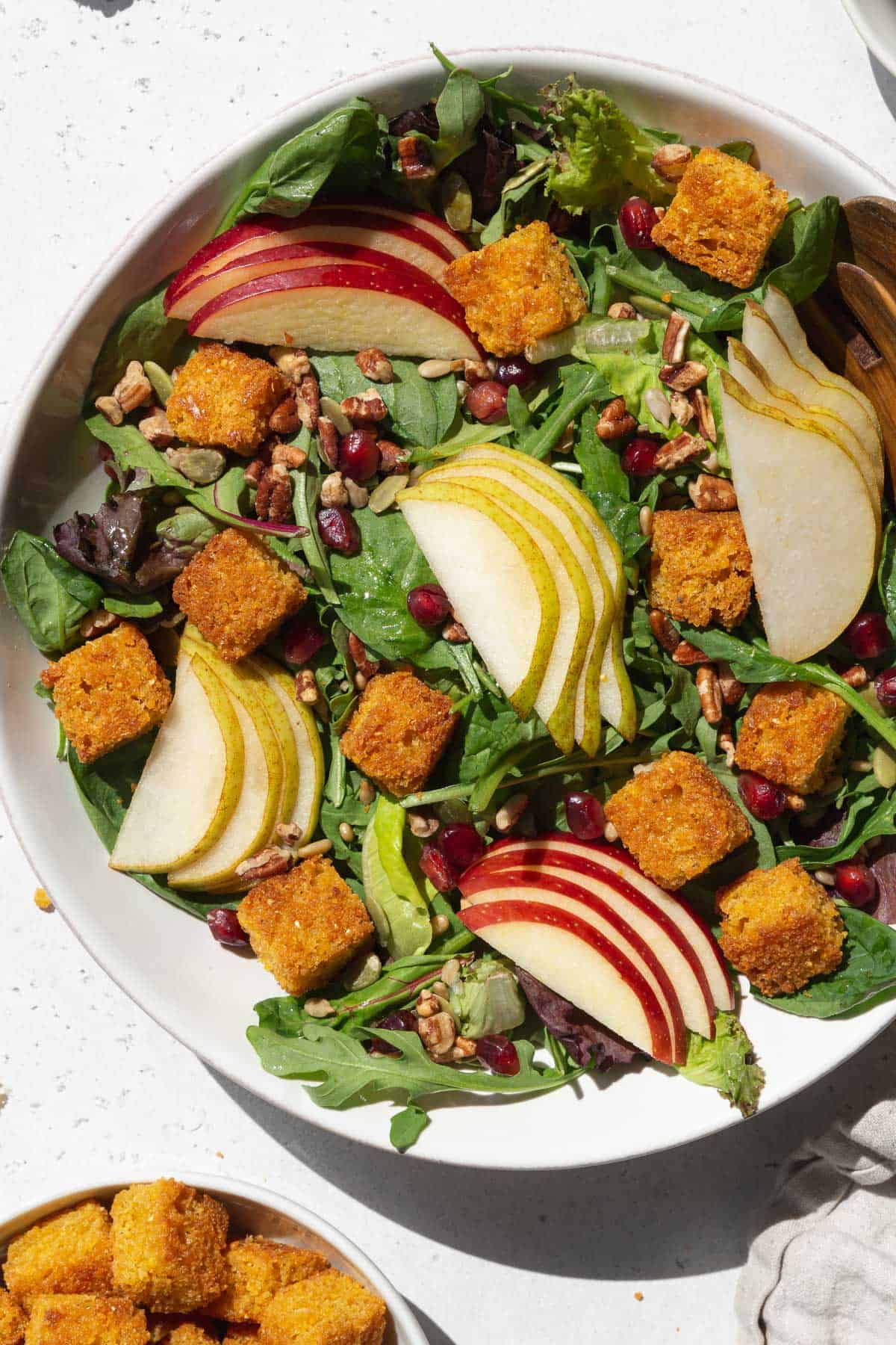 A large bowl of salad with sliced apples, pears, and cornbread croutons.