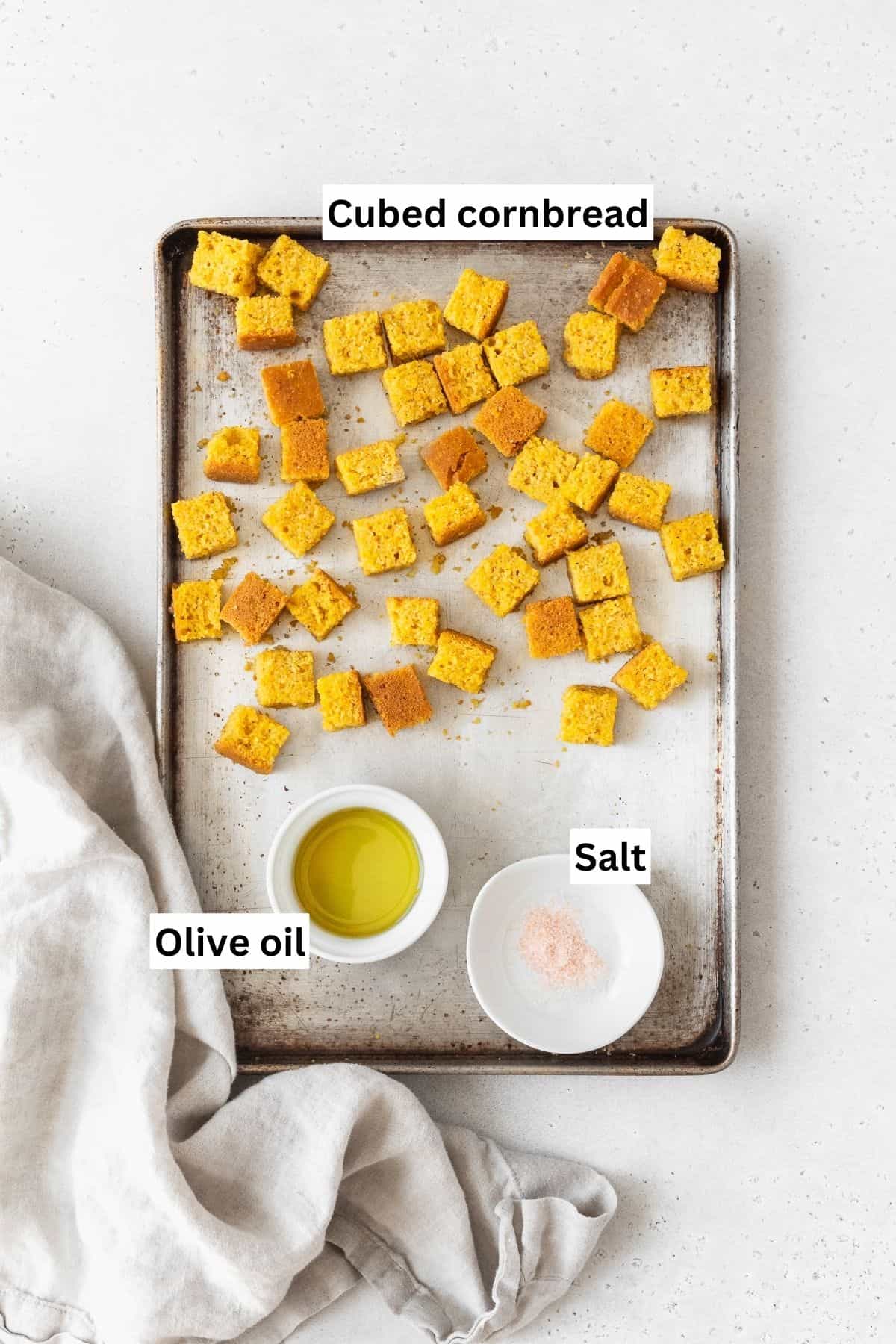 A baking sheet with cubed cornbread, olive oil, and salt.