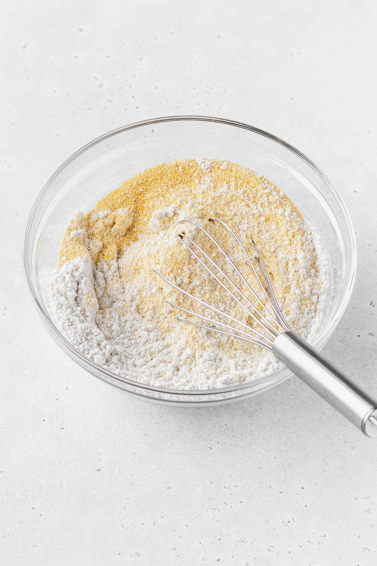 Whisking the dry cornbread ingredients together in a glass mixing bowl.