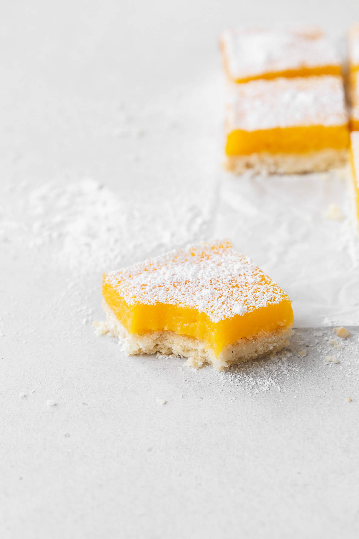 A dairy-free lemon bar with a bite taken out of it sitting on the counter with powdered sugar.