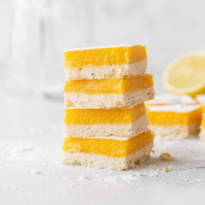 Stacked dairy-free lemon bars on the counter with powdered sugar and crumbs.