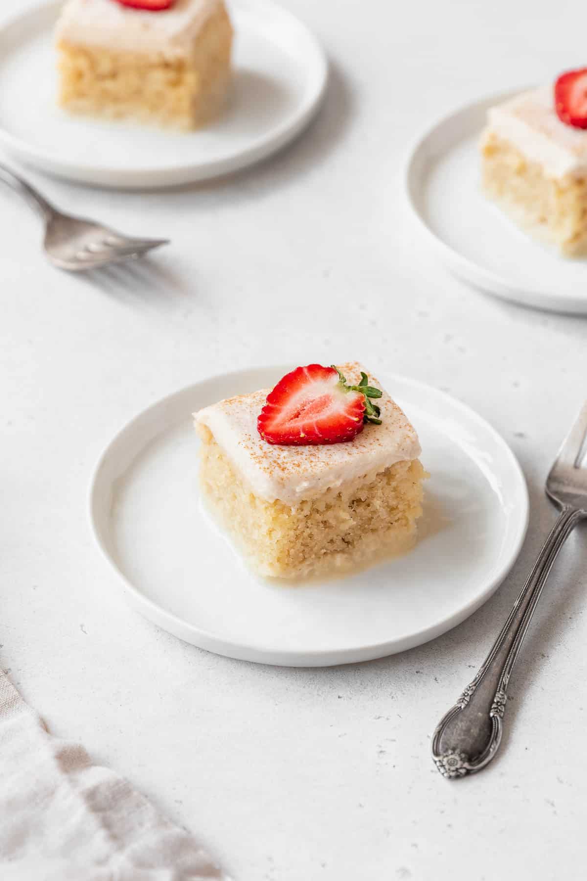 Three slices of gluten-free tres leches cake on white dessert plates with strawberries.