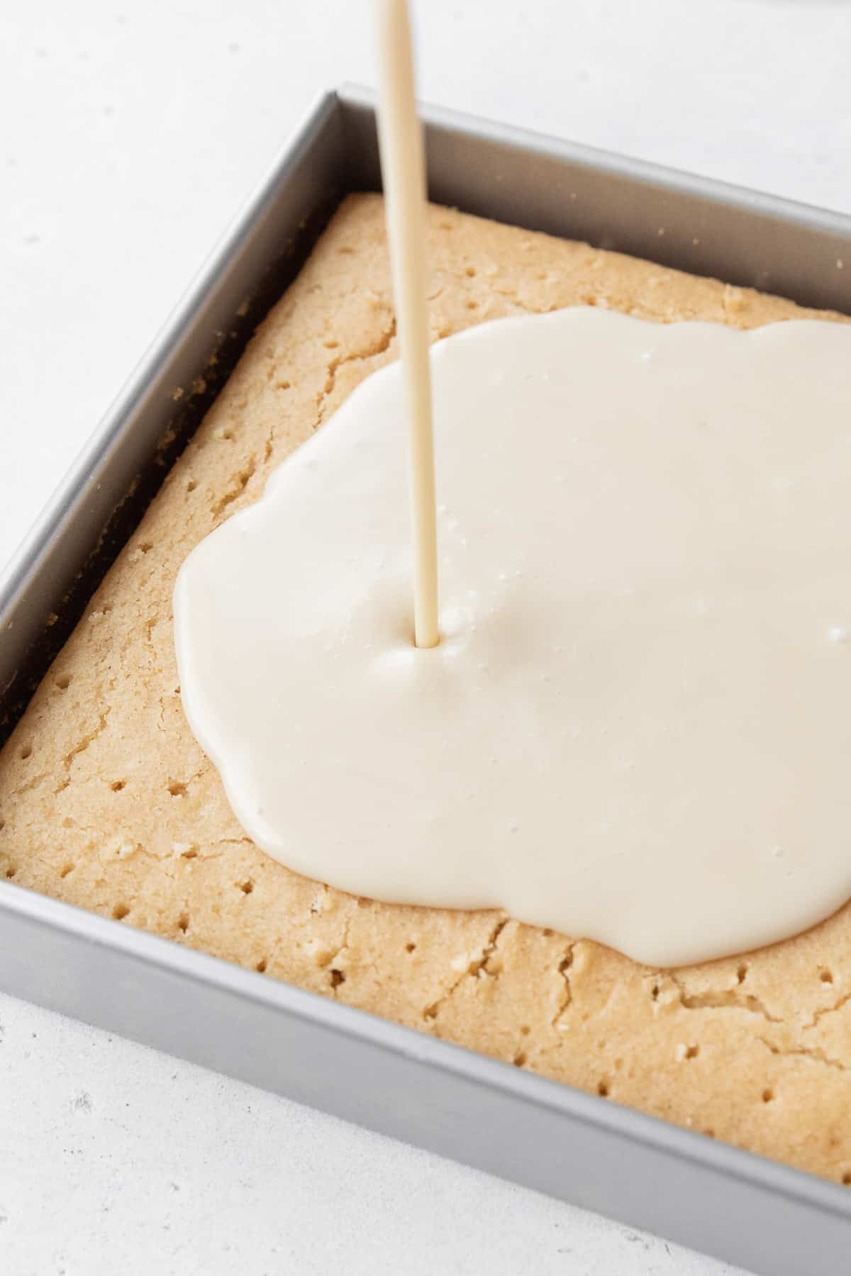 Pouring the dairy-free tres leches milk soak over the cake with poked holes in it.