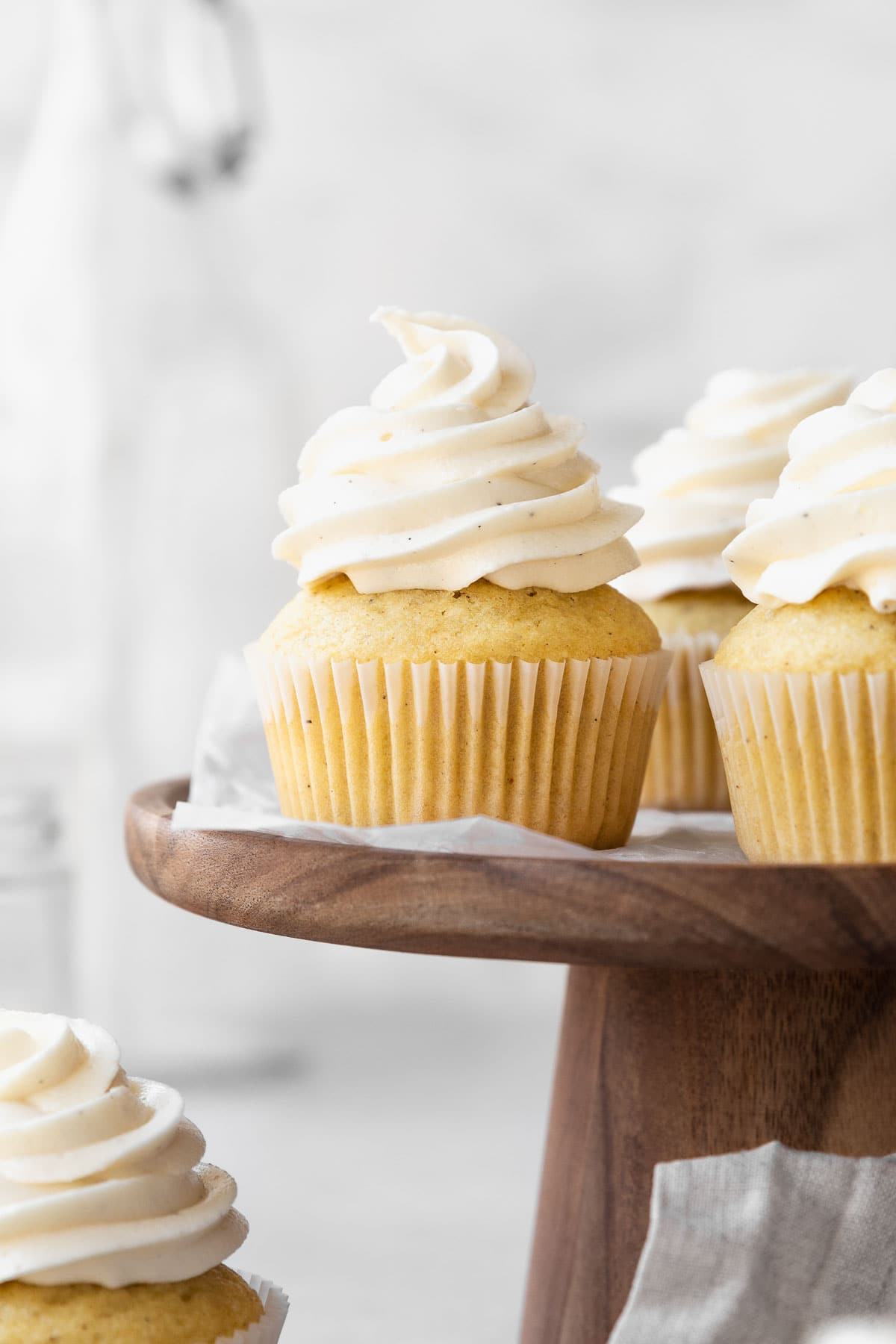 Dairy-free vanilla cupcakes on a wooden cake stand.