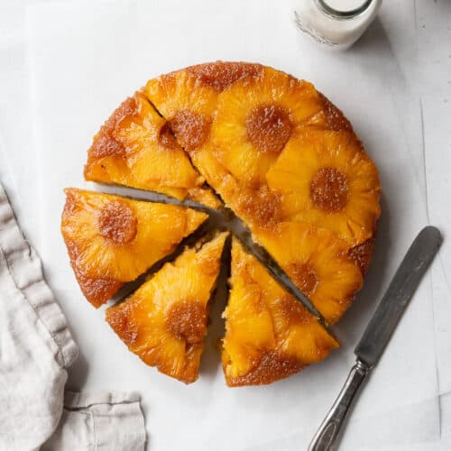 A sliced gluten-free pineapple cake on a white surface with a linen and a knife.