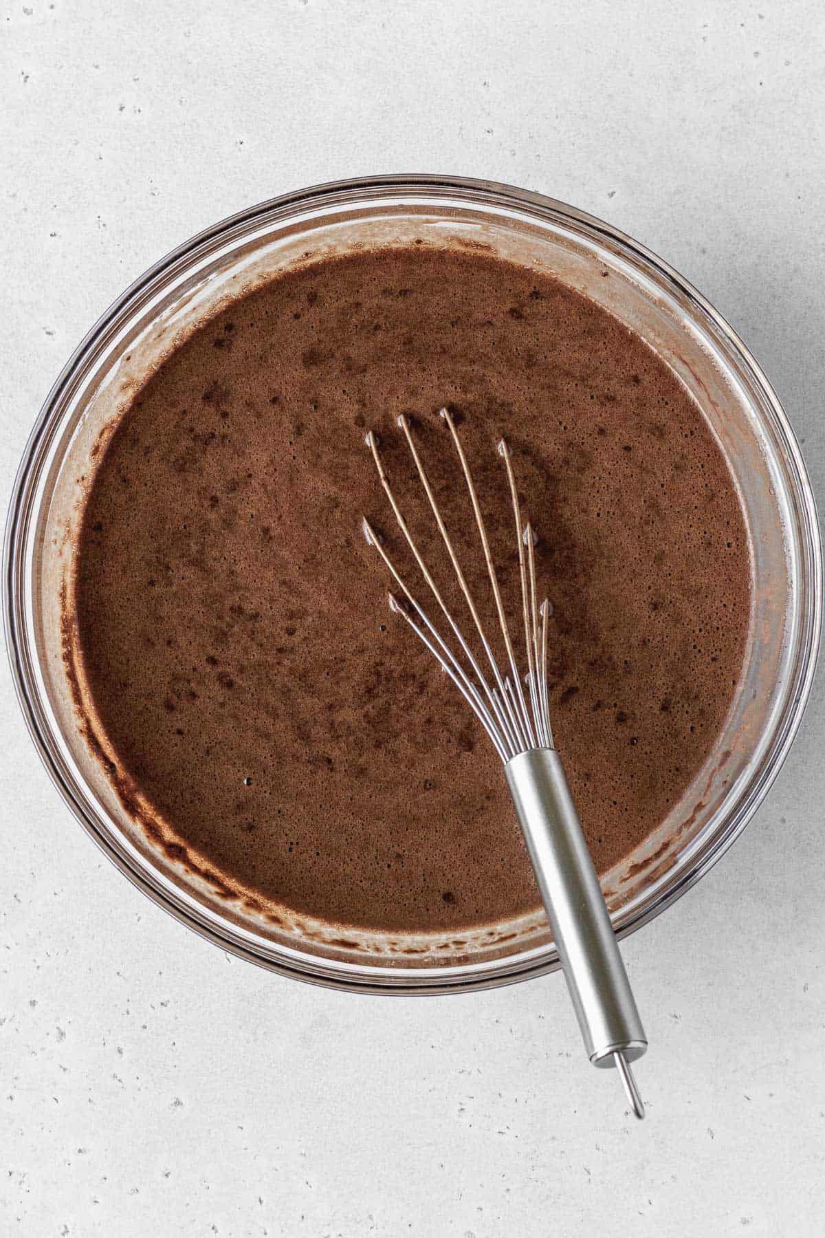 Gluten-free German chocolate cake batter in a glass bowl with a whisk inside.