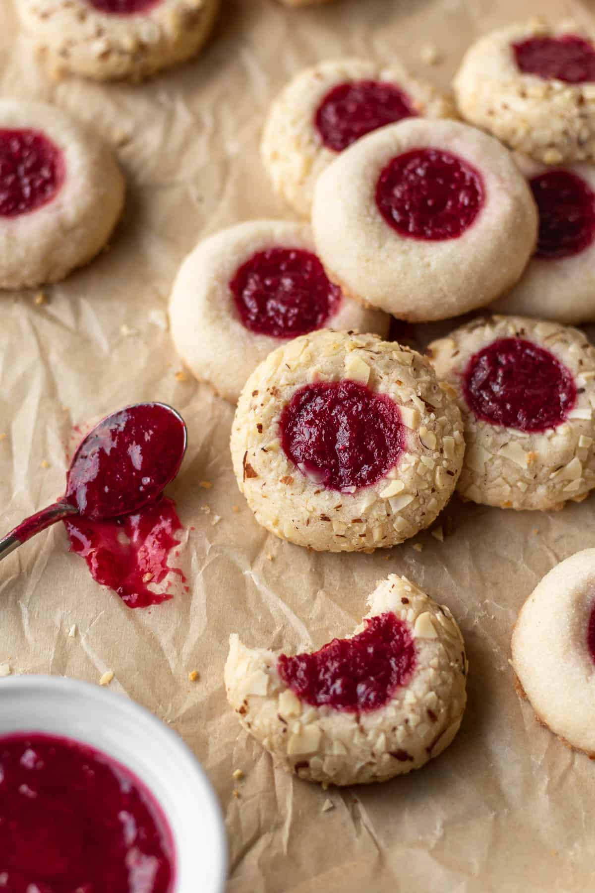 Gluten free thumbprint cookies next to a small spoon of jam on a brown parchment paper.