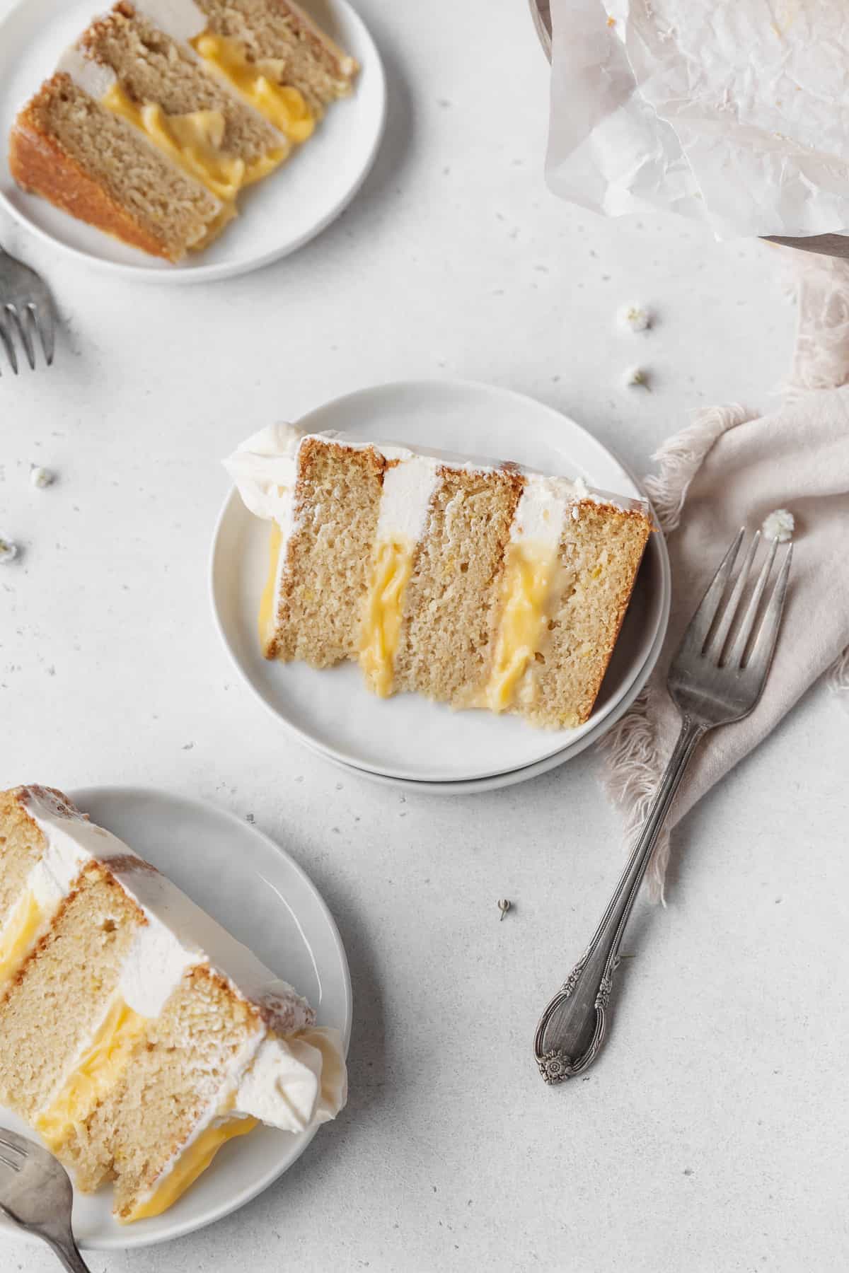 Overhead shot of 3 slices of dairy-free lemon curd layer cake on white dessert plates with silver forks.
