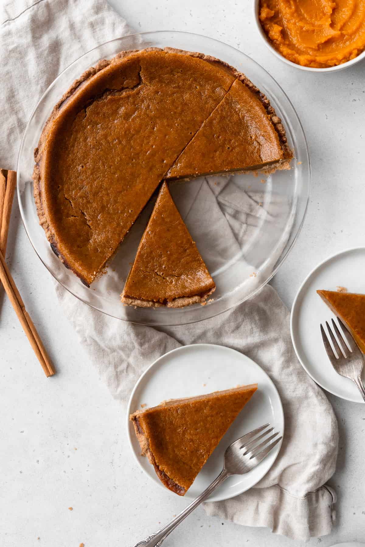 A sliced egg-free pumpkin pie on a natural linen with small plates of pie slices placed next to it.