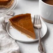 Square image of a slice of eggless pumpkin pie on a white dessert plate and a silver fork placed beside it.