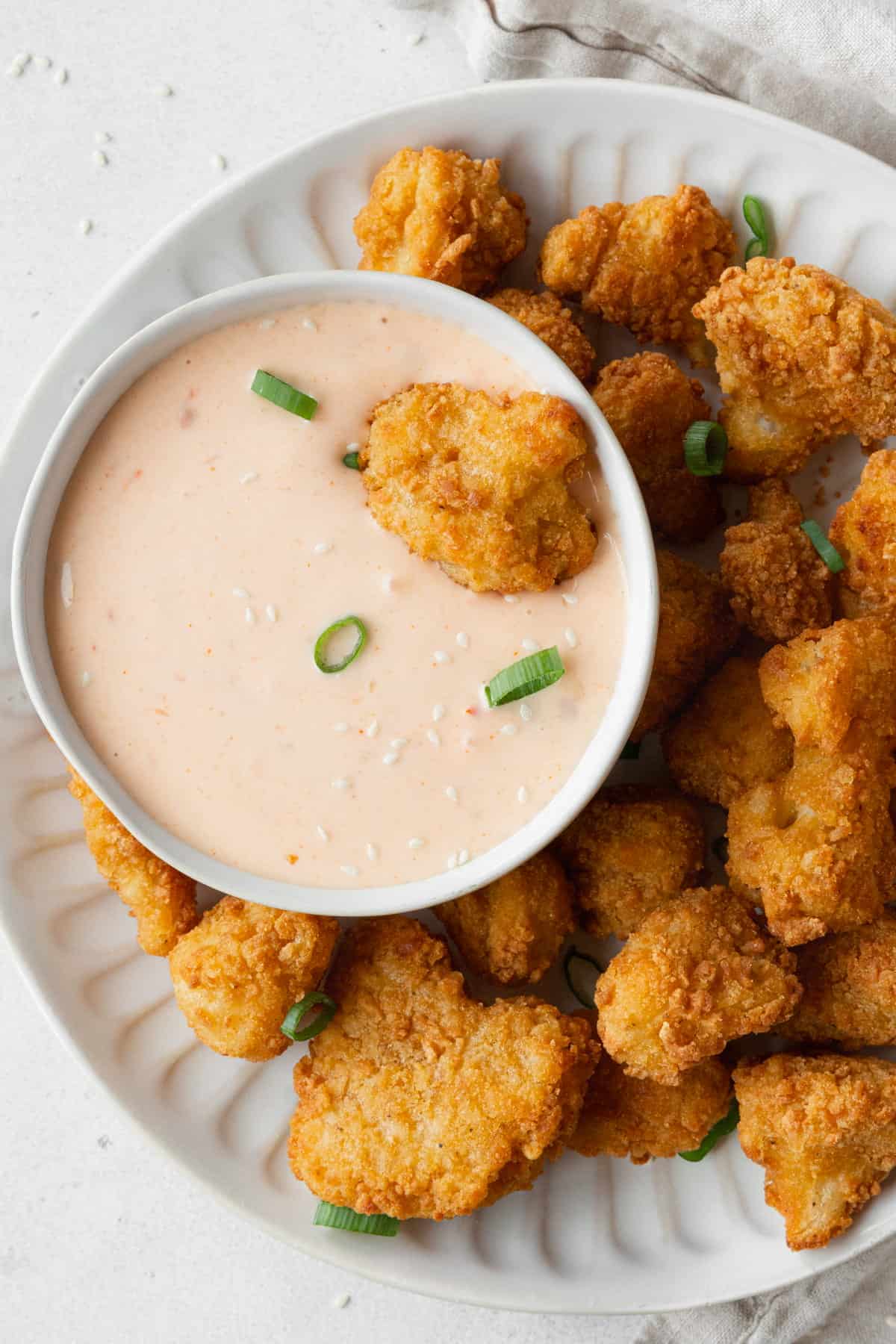 A plate of cauliflower bites with a bowl of bang bang sauce.