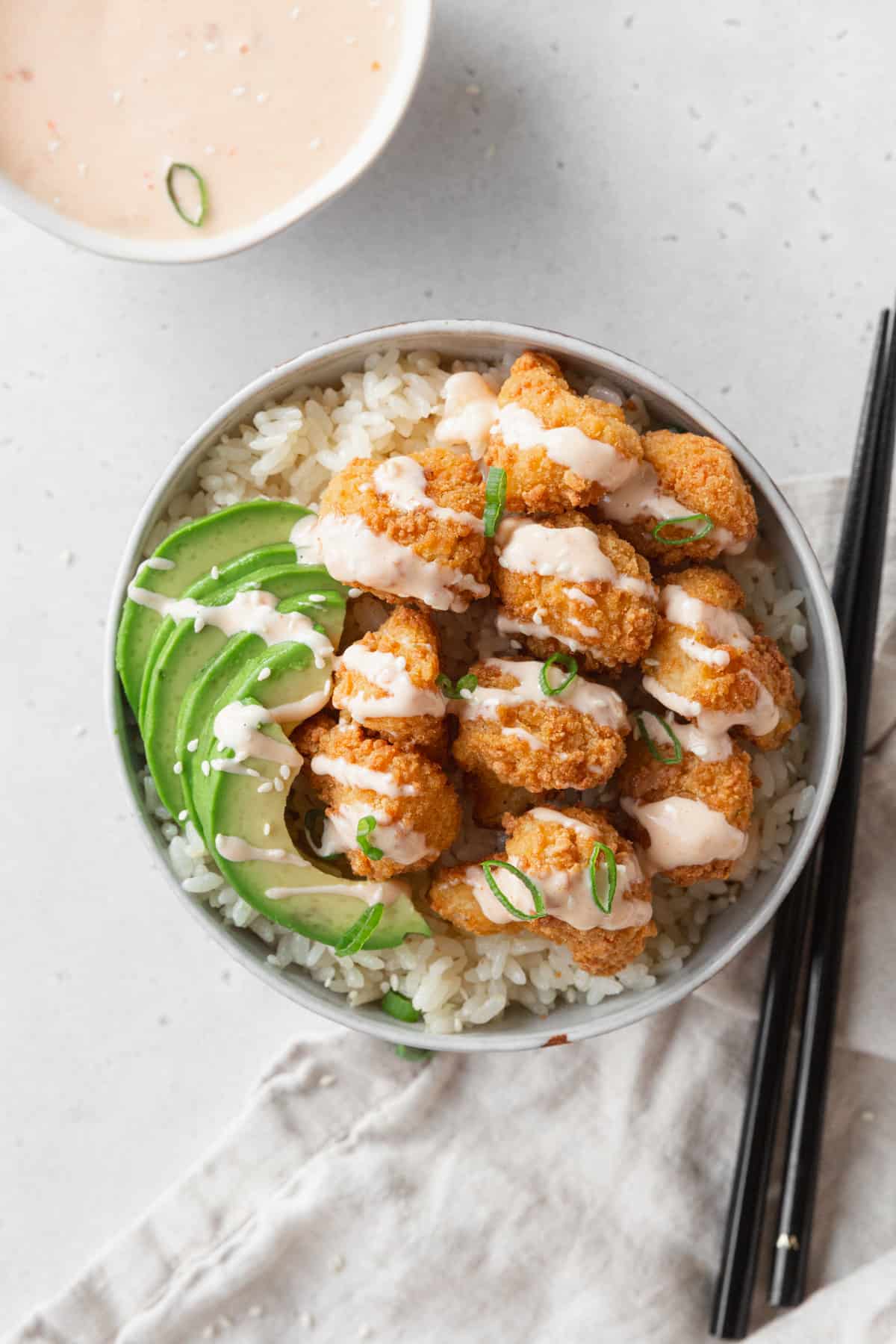A bowl of coconut rice with bang bang cauliflower and avocado on top.
