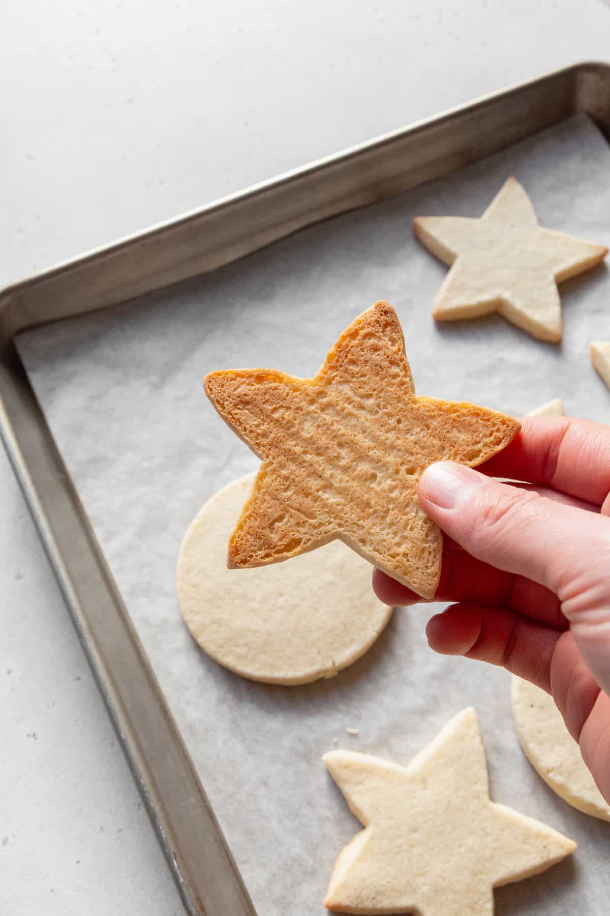 A hand holding a star-shaped sugar cookie, showing the golden color of the bottom of the cookie.