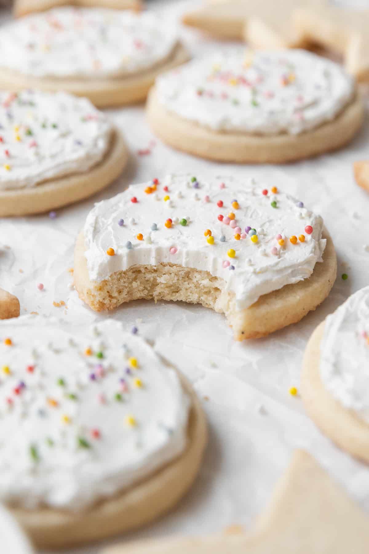 A bitten frosted gluten-free sugar cookie with sprinkles surrounded by more cookies.