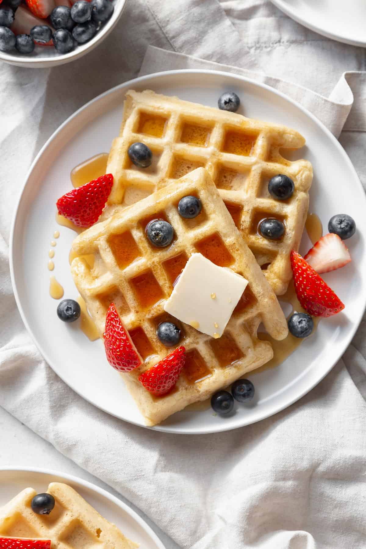 Gluten free waffles on a plate with butter, blueberries, and strawberries on top.