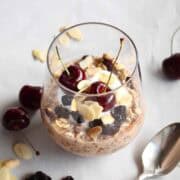 Overnight oats in a glass topped with yogurt, dried cherries, sliced almonds, and two fresh cherries on top.