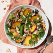 Peach salad in a white bowl on a peach colored linen, with a spoon and fork on the side.