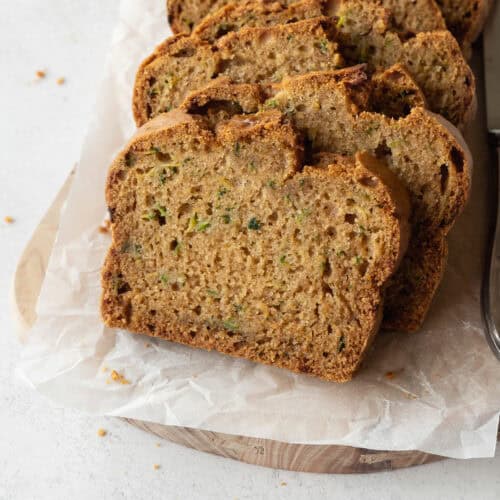 Slices of gluten-free zucchini bread on a wooden board lined with parchment paper.